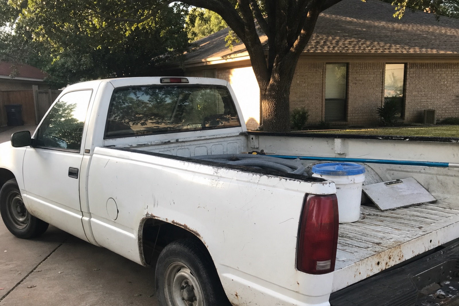 Weathered white work truck parked in a Fort Worth driveway with pool hose, bucket, and clipboard in the bed.