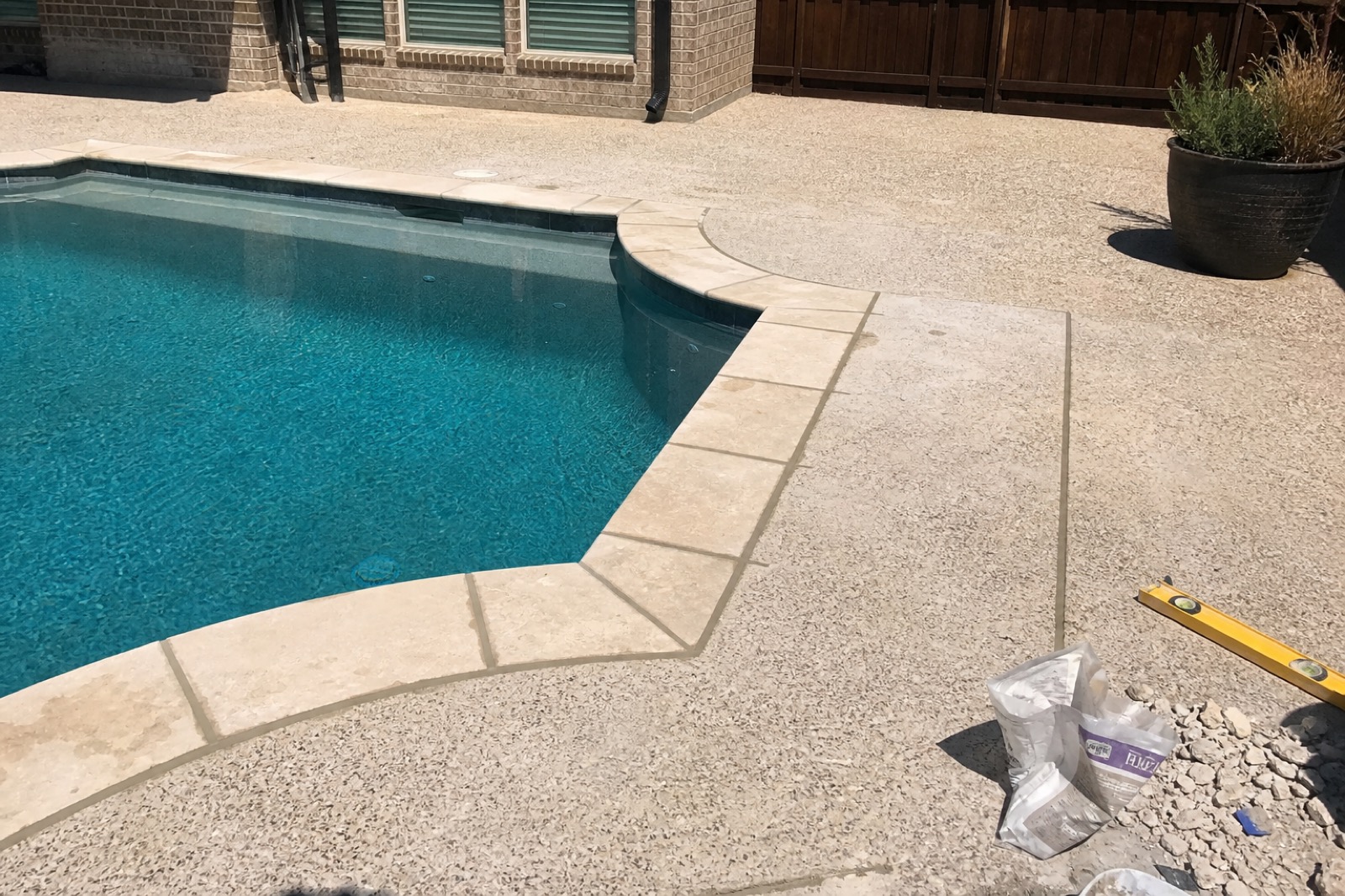 A Fort Worth residential pool with freshly installed light travertine coping stones, mortar joints still curing.